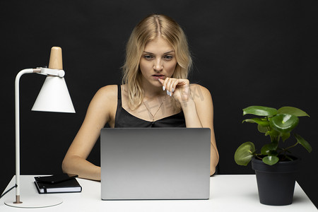 有魅力的自由职业女性的画像，她身穿黑色 T 恤，在一间有黑墙的工作室里拿着笔记本电脑。
