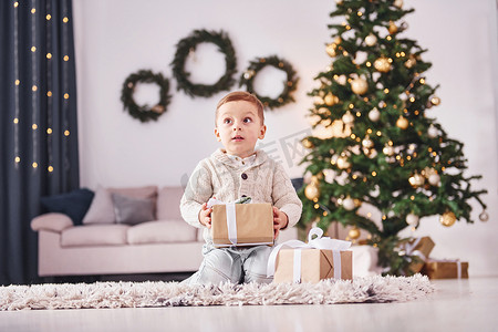 手里拿着礼盒的小男孩在家里有新年装饰和绿树