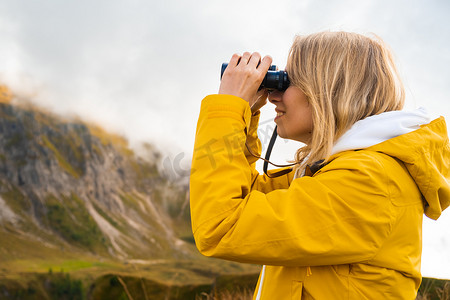 在云层覆盖的山中通过双筒望远镜看旅行女孩的侧视图