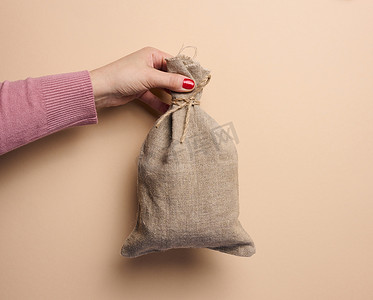 一个女人的手拿着一个米色背景的帆布包，补贴的概念，帮助