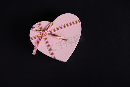 静物与一个心形的粉红色礼品盒，黑色背景上系着蝴蝶结。