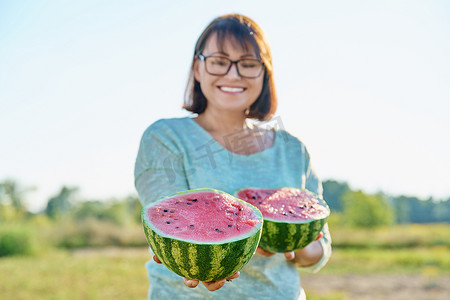 微笑的女人手里拿着半个成熟的西瓜，户外