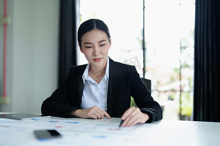 一位体贴的亚洲女商人的肖像，她正在使用办公桌上的平板电脑查看财务报表并制定营销计划