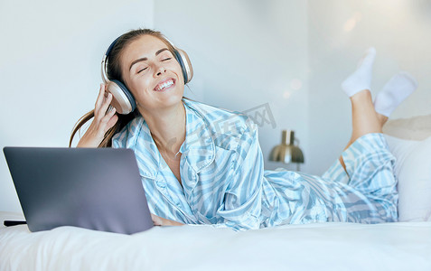 耳机、笔记本电脑和躺在床上的女人，在早晨的阳光或镜头光晕中播放心理健康、放松和健康的音乐。