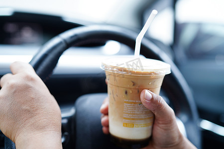泰国曼谷 — 2022年5月15日，亚洲女司机拿着冰咖啡杯在车里喝，很危险，有发生事故的风险。