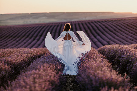 穿着白色连衣裙和草帽的快乐女人在日出时漫步穿过薰衣草田，沉浸在宁静的氛围中。