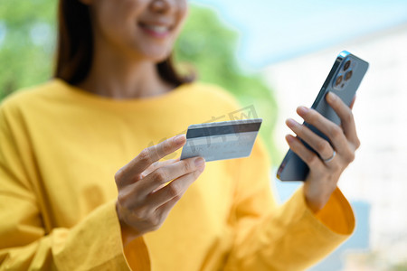 手持手机银行摄影照片_年轻女性手持信用卡并使用智能手机在线支付或查看她的银行账户