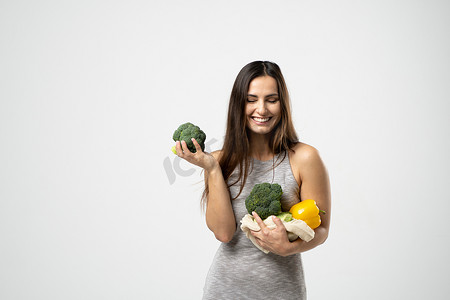 蔬菜免费摄影照片_微笑的黑发女孩拿着西兰花和网状购物袋，里面装着蔬菜，没有塑料袋的蔬菜。