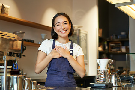 爱的物语摄影照片_友善微笑的亚洲女咖啡师，手牵手，对客户表示感谢，爱咖啡馆里的客人，穿着制服围裙