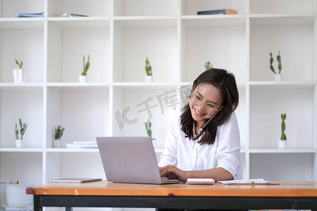 年轻亚洲女商人的画像在家庭办公室用智能手机写笔记本电脑。