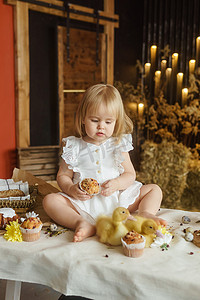 一个小女孩坐在复活节桌上，和可爱的毛茸茸的小鸭子玩耍。