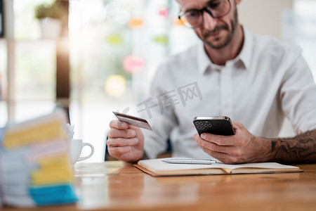 一名男子从信用卡背面读取信息并在智能手机上输入信息，以便在家中进行在线购买。