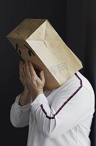 哭的表情符号摄影照片_悲伤的男人头上顶着一个袋子，画着哭泣的表情符号。