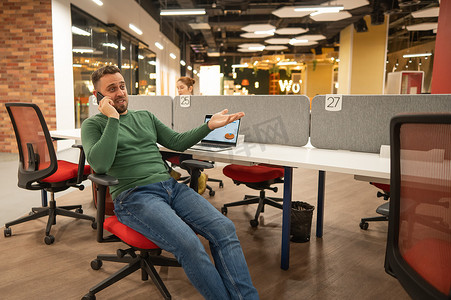 在现代联合办公空间的办公桌前，留着胡子的白种人用智能手机聊天。