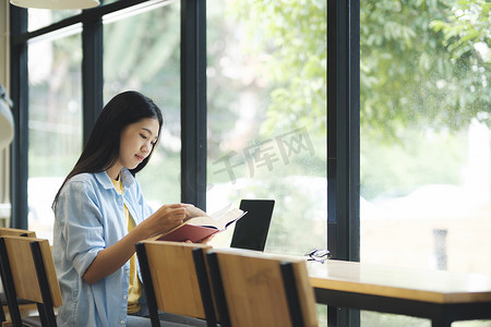 女人坐着摄影照片_年轻的亚洲女人坐着看书。