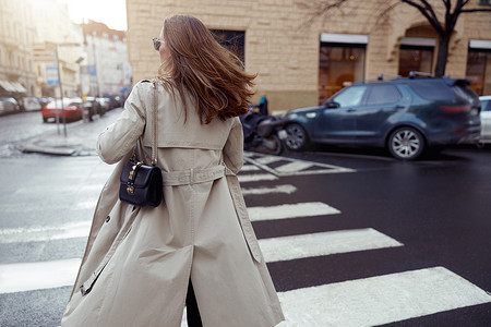 马路背景摄影照片_在城市建筑的背景下，穿着时髦服装的女性的背影穿过马路