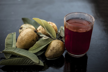 红色透明玻璃摄影照片_红番石榴或 amarood 或 jamrukh 有机果汁的特写，在透明玻璃杯中，木表面上有生番石榴及其叶子。