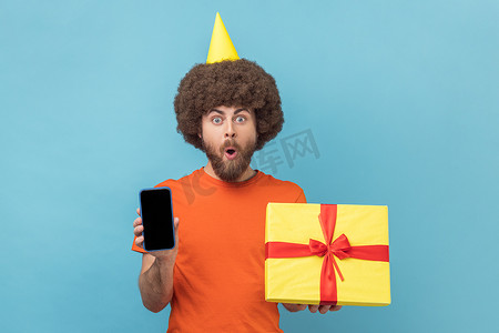 男士促销摄影照片_男士派对锥拿着礼品盒和带空白显示屏的手机进行促销。