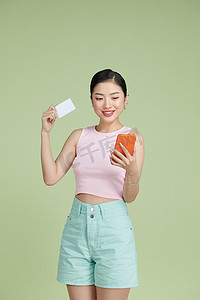 快乐的年轻女孩拿着塑料信用卡，同时拿着绿色背景中突显的手机