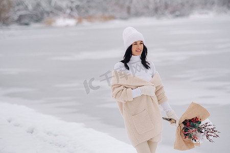 一个穿着米色开衫和冬花的女孩在下雪的季节在大自然中漫步。
