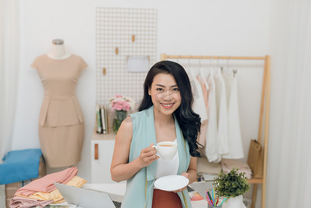 美丽的年轻亚洲时装设计师女商人在她的工作室喝咖啡时的肖像