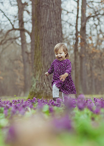 穿着彩色裙子的金发婴儿在开着鲜花的林间空地奔跑