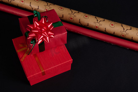 静物圣诞礼品盒，装饰有绿色丝带和红色蝴蝶结，黑色背景上有包装纸。