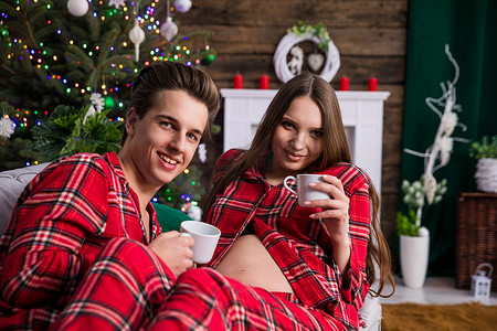 在圣诞装饰和圣诞树的背景下，一对怀孕的夫妇看着镜头。