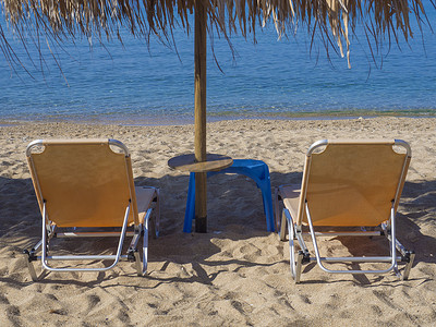 在希腊沙滩上用绿松石清澈的海水关闭两张带太阳伞的黄色空日光浴床