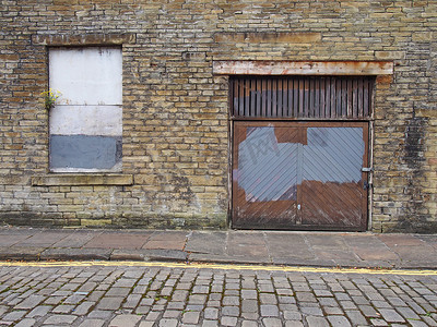 在一条空荡荡的街道上，一个废弃的废弃工业地产的前视图，上面有木板的窗户和破旧的砖墙