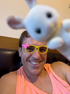 戴玩具眼镜的男人和一只玩具兔子坐在床上
