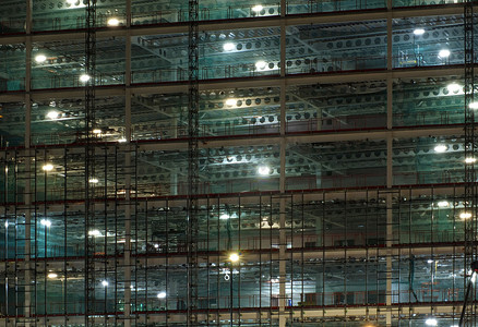 夜间大型建筑工地的全框架视图，由带有大梁和施工升降机的明亮工作灯照亮