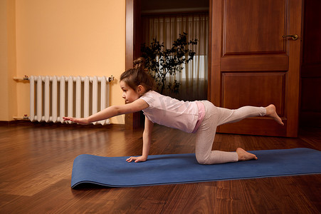 侧视图活跃的儿童女孩在健身垫上练习瑜伽。