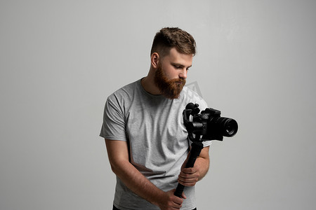 专业大胡子摄影师、电影摄影师、摄影师在万向节稳定器上使用相机的侧视图，白色背景上的替身。