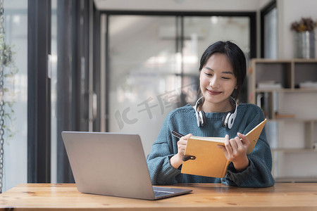 年轻成年快乐微笑的亚洲学生戴着耳机在大学校园或虚拟办公室使用笔记本电脑在在线聊天会议上交谈。