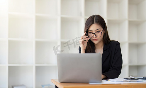 坐在办公桌前的漂亮女商人拿着眼镜，周围是电脑笔记本电脑、文书工作、计算器、与财务、办公室税务相关的文件