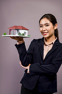 穿着正式西装的年轻亚裔女性拿着房子模型。