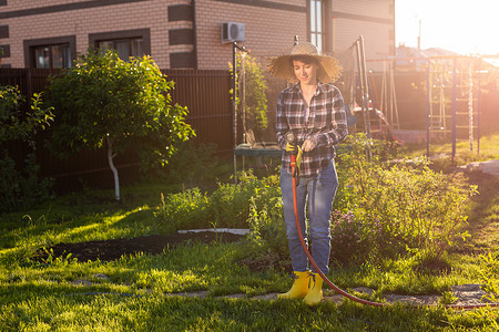 在阳光明媚温暖的夏日，穿着工作服的白人女园丁在她的菜园里浇花。