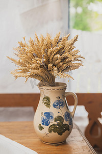 秋天花瓶摄影照片_旧小屋里放着一束小麦的陶瓷壶