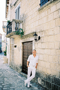 身穿白衬衫的微笑男子倚靠在一座旧石屋旁