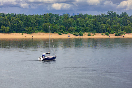 在河岸和绿地的映衬下，帆船在雨中漂流在河中央。