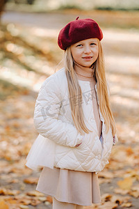 一个戴着帽子的快乐女孩在秋天的公园里散步