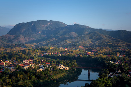 横穿摄影照片_下午，从高处俯瞰老挝琅勃拉邦市，南康河横穿，周围环绕着茂密的热带雨林。