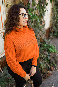 秋天的画像中，一位戴着时尚眼镜、身穿时尚橙色针织毛衣、背景为树叶的迷人年轻女子的画像。