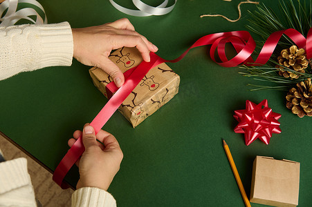 特写女人用一条闪亮的红丝带，用鹿图案的包装纸包裹圣诞礼物。