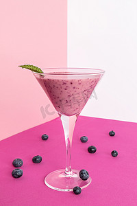 粉色漱口杯摄影照片_蓝莓冰沙杯，粉色、白色和紫红色背景上有几个蓝莓。