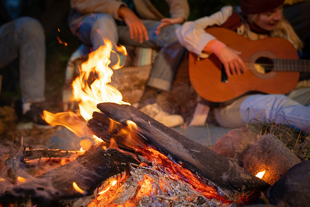 无法辨认的朋友们在晚上玩音乐和在大自然中享受篝火露营的乐趣
