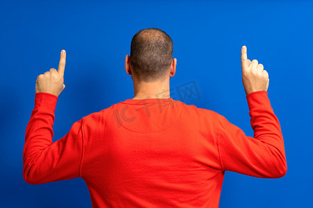 一个患有早期脱发的男人的肖像，从后面举起双手，食指向上，孤立在蓝色背景中。