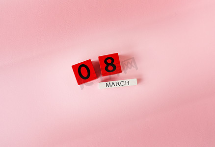 妇女节背景红色摄影照片_粉红色背景上刻有“3 月 8 日”字样的木制立方体，刻有妇女节快乐的字样。