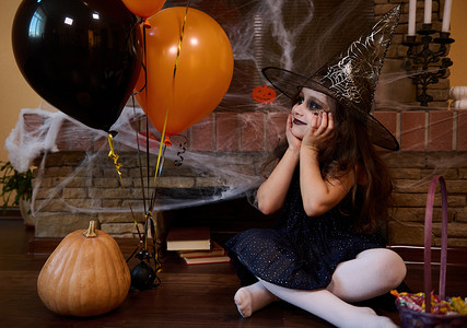 巫师摄影照片_戴着巫师帽、化着面部艺术妆的漂亮小女孩，在可怕的哥特式室内享受万圣节派对